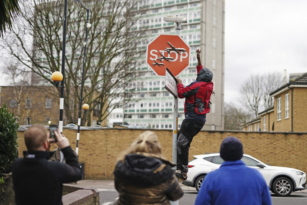 Una persona retira una obra de arte de Banksy que parece mostrar tres drones sobre un cartel de Stop que fue develado en la intersección de las calles Southampton Way y Commercial Way en Peckham, sureste de Londres, viernes 22 de diciembre de 2023. (Aaron 