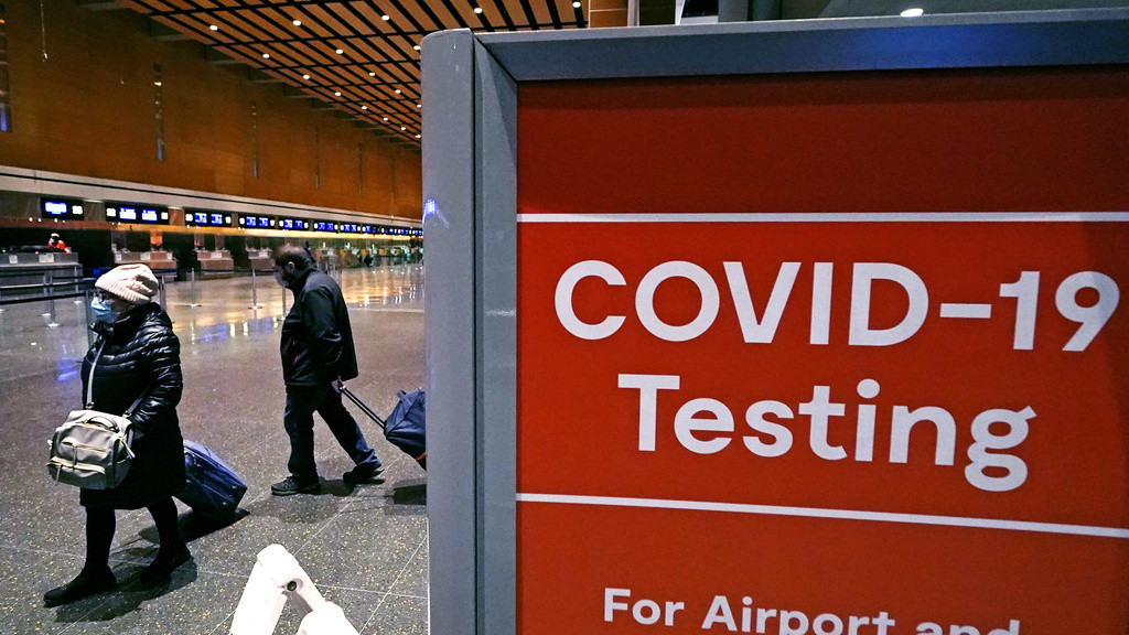 Viajeros pasan junto a un letrero cerca de un centro de pruebas de COVID-19 en la Terminal E del aeropuerto Logan el 21 de diciembre de 2021, en Boston.(AP Foto/Charles Krupa, Archivo)