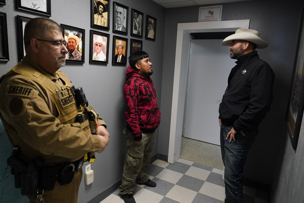 Un migrante mexicano recientemente detenido, mientras el sargento Manuel Jimenez permanece a un costado, en el Departamento de Policía del condado Terrell, el jueves 21 de marzo de 2024, en Sanderson, Texas. (AP Foto/Erik Verduzco)