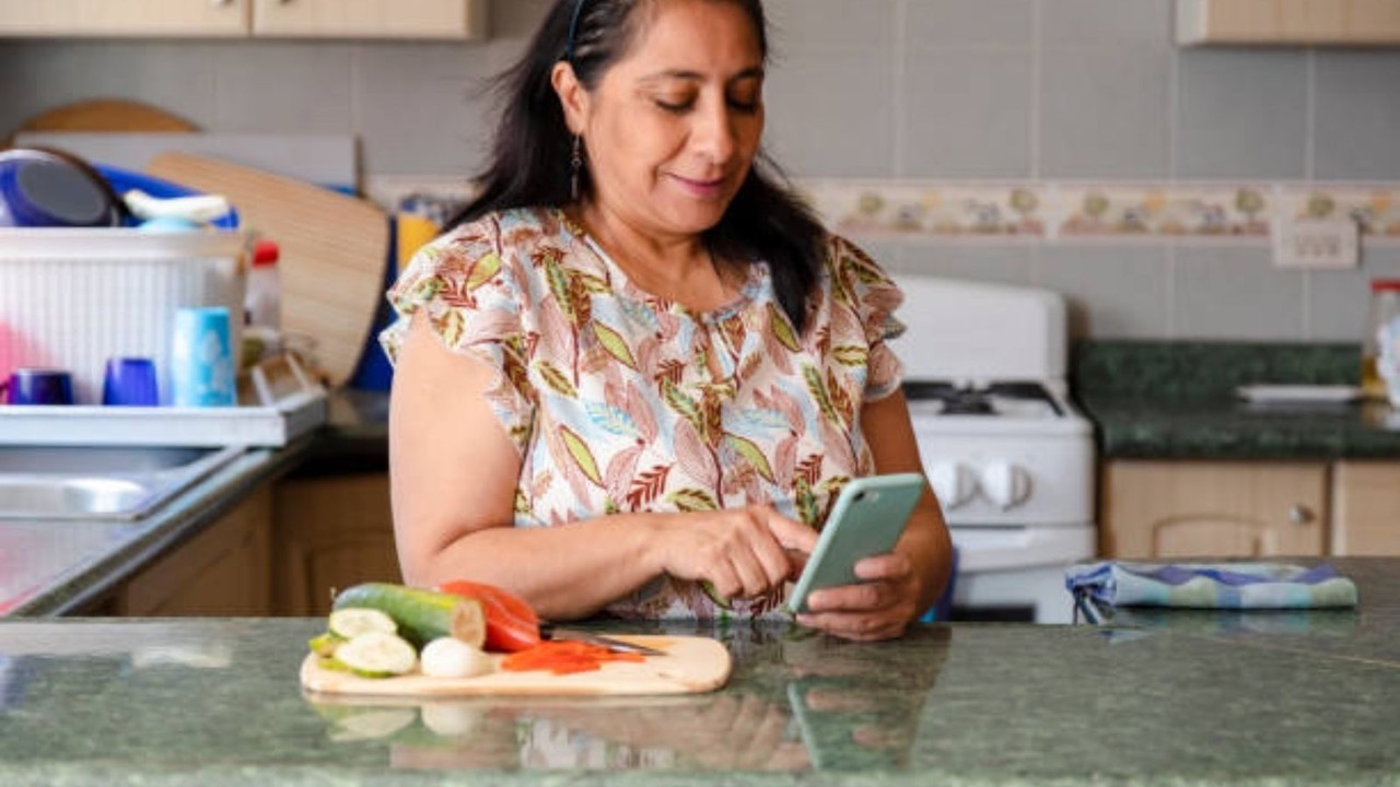 Mujer revisando su celular mientras cocina. Foto: Pixabay.