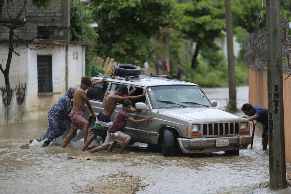 Varias personas empujan una camioneta atascada en una calle inundada por el paso del huracán John, el viernes 27 de septiembre de 2024, en Acapulco, México. (AP Foto/Bernardino Hernández)