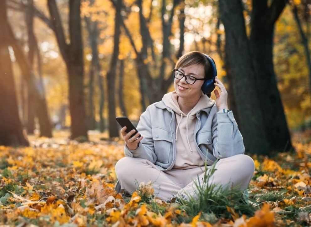 Mujer escuchando música abajo de un árbol en otoño. Foto: Los 40.