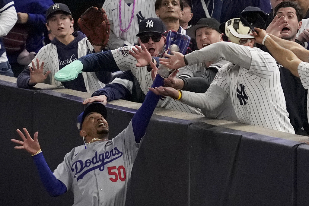 Fanáticos interfieren en un elevado de foul atrapado por el jardinero derecho Mookie Betts de los Dodgers de Los Ángeles ante los Yankees de Nueva York. (AP Foto/Ashley Landis)