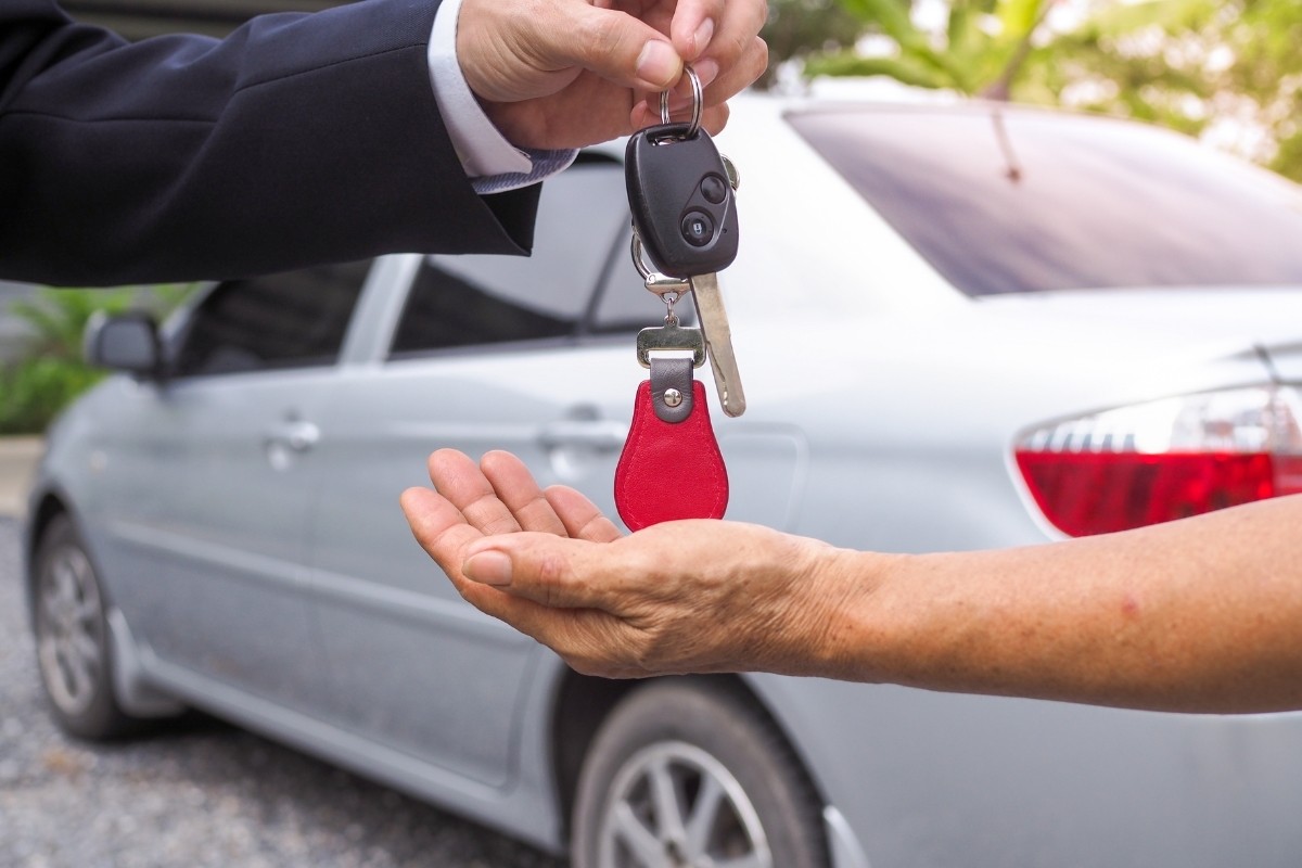 Vehículo y persona recibiendo llave de automóvil. Foto: Canva