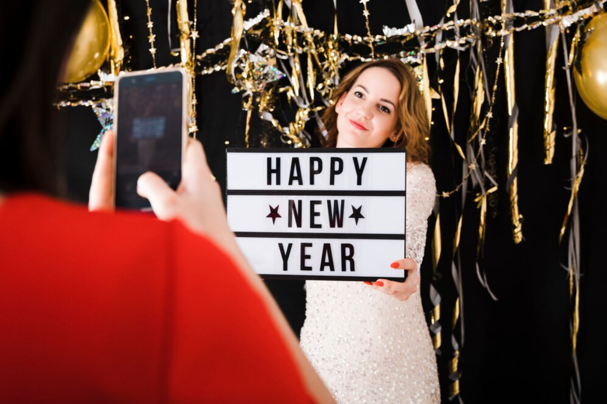 Mujer sosteniendo un cartel de Año Nuevo, mientras es fotografiada.     Foto: Freepik, redimensionada en Canva.