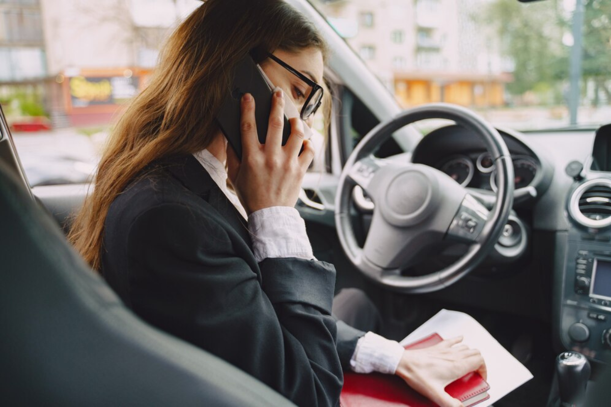 Conductora de vehículo usando su celular. Foto: Freepik, editada en Canva.