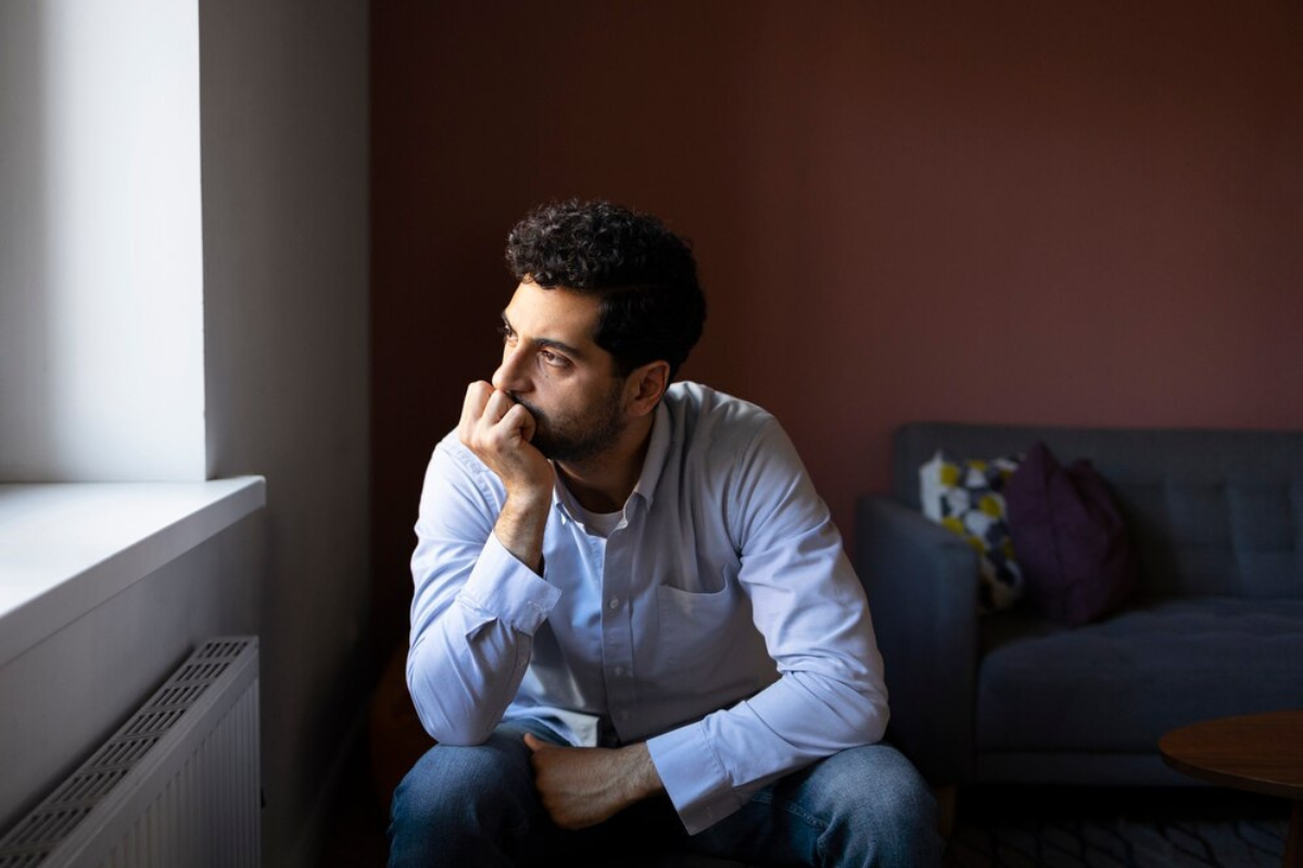 Hombre triste viendo hacia la ventana.    Foto: Freepik, redimensionada en Canva.