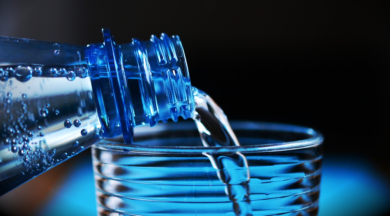 Botella de agua llenando un vaso de cristal. Fondo azul marino. Foto: pixabay.com