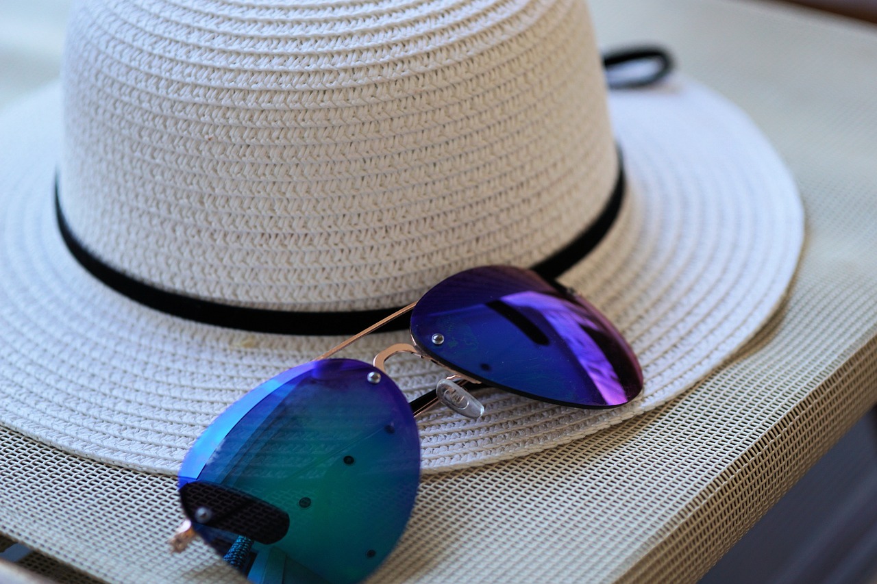 imagen de un sombrero de paja, tipo fedora, color blanco, junto a unas gafas de sol. Foto: pixabay.com