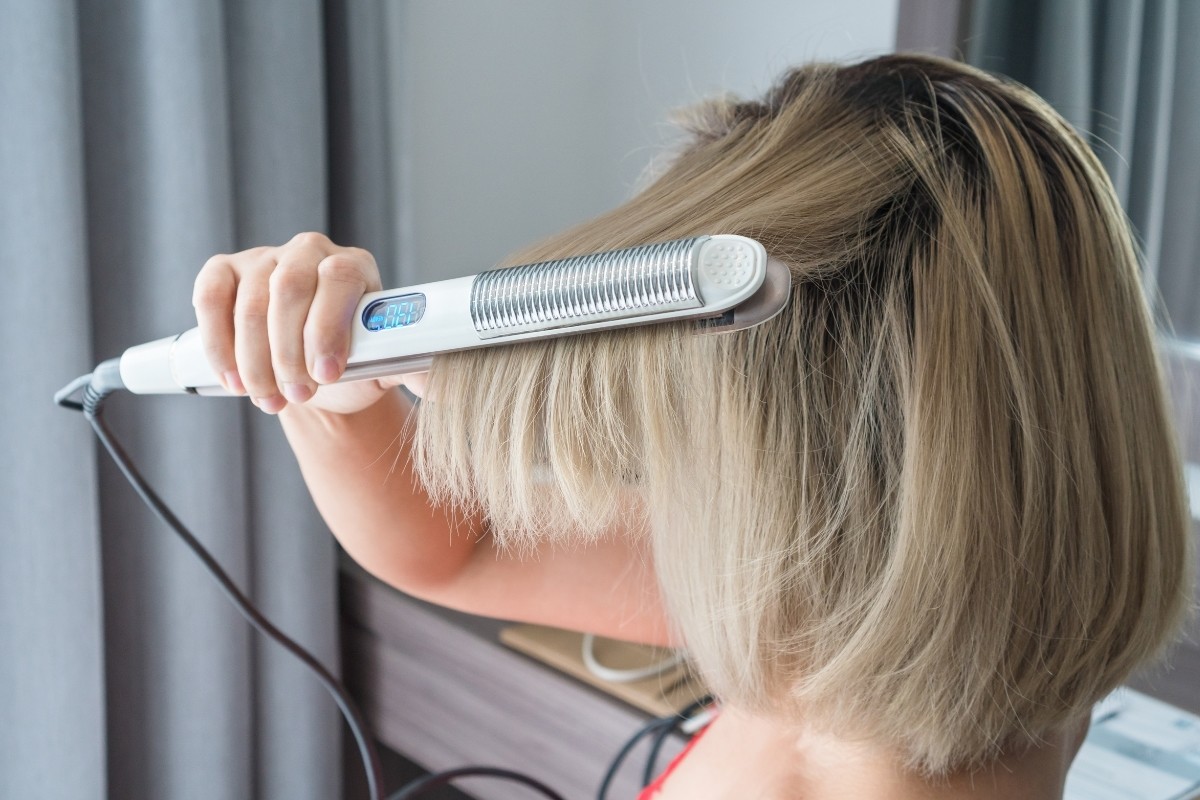 Mujer alaciando su cabello. Foto: Canva