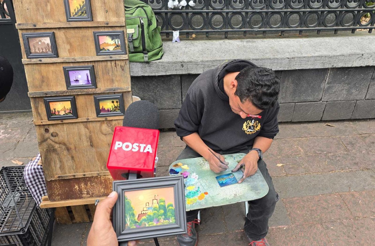 Julio César Hernández pintando uno de sus mini cuadros frente al Bosque de Chapultepec, y al frente un micrófono de POSTA.     Foto: Mario Flores