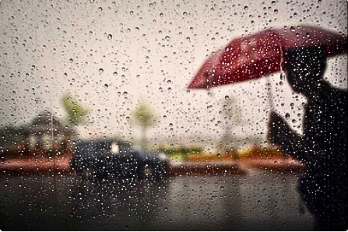 Lluvia fuerte cayendo sobre una calle, en la que pasa un automóvil y una persona sosteniendo un paraguas. Foto: Especial