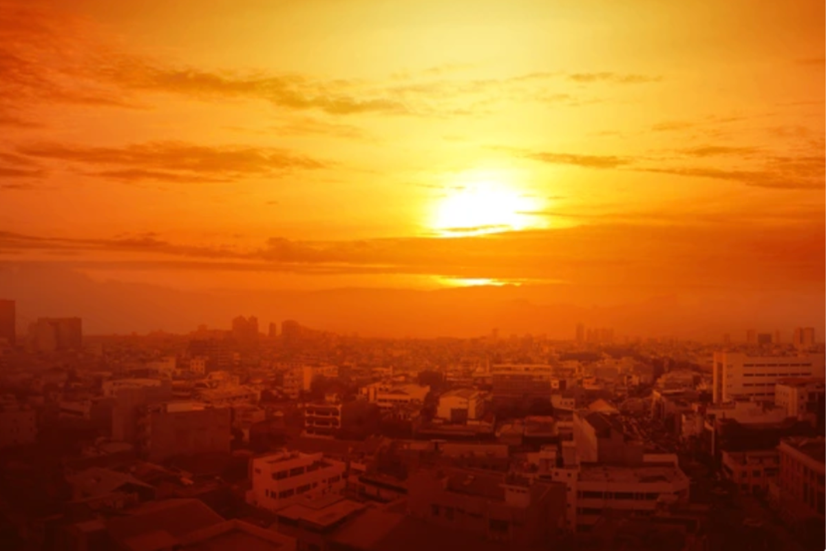 Foto panorámica de una ciudad, en tonos anaranjados, mientras al fondo se ve el sol entre nubes. Foto: leolintang