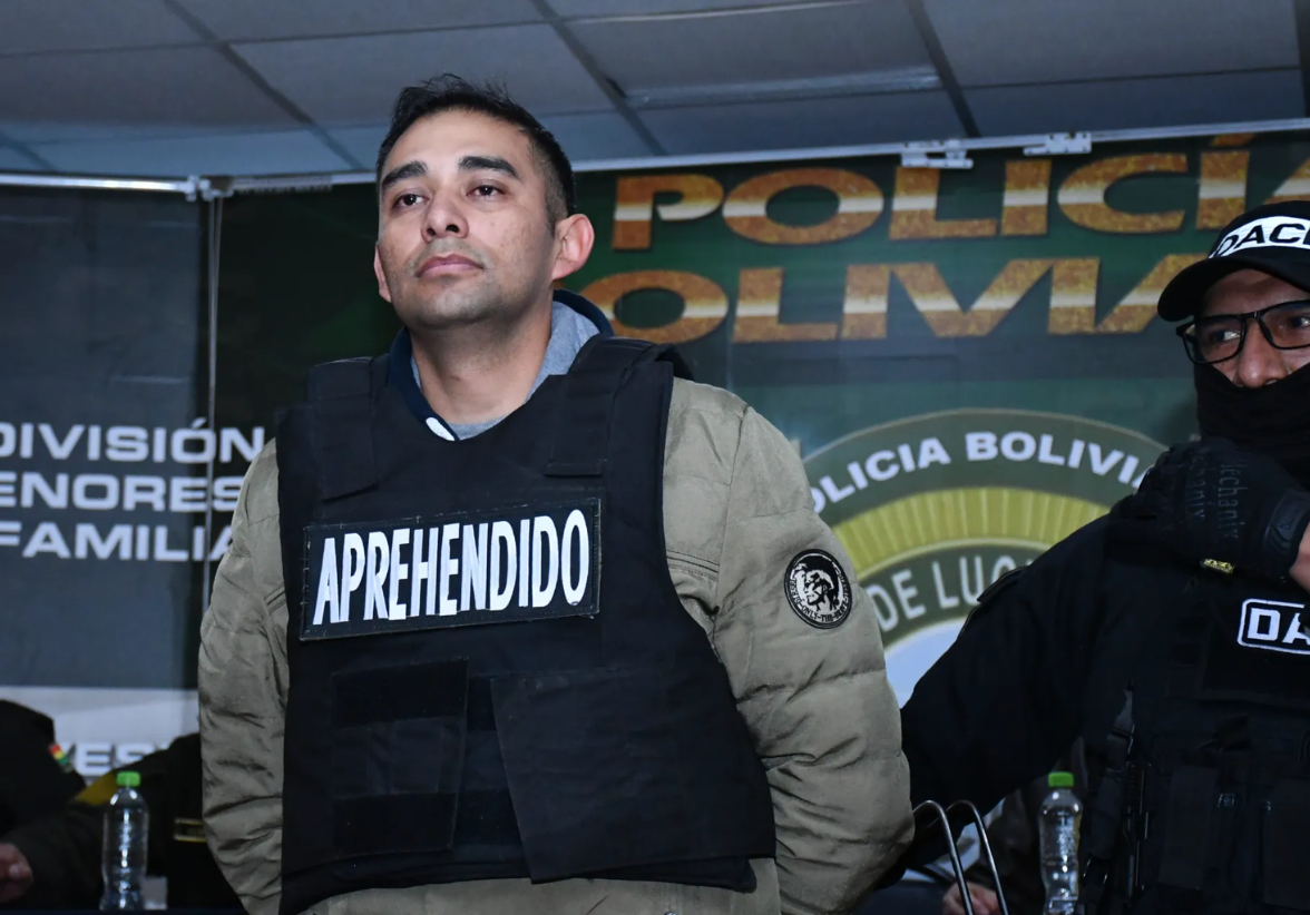Un agente de la Dirección de Análisis Criminal e Inteligencia (DACI) de Bolivia escolta al capitán de infantería Miguel Burgos este viernes, durante su presentación luego de su arresto en La Paz. Foto: EFE