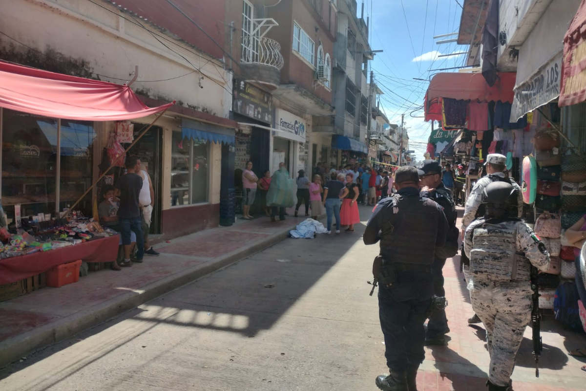 Elementos de seguridad resguardando la zona, mientras permanece el cuerpo del ejecutado en el piso y rodeado de personas. Foto: Armando de la Rosa